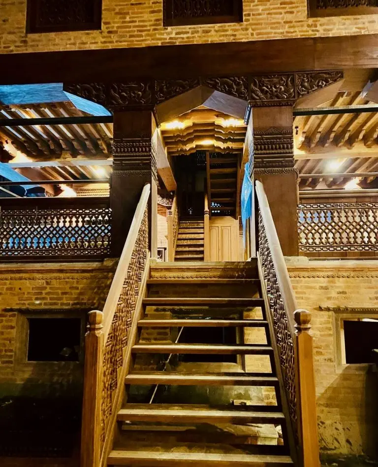 Carved Newari staircase rising into the lit courtyard at night