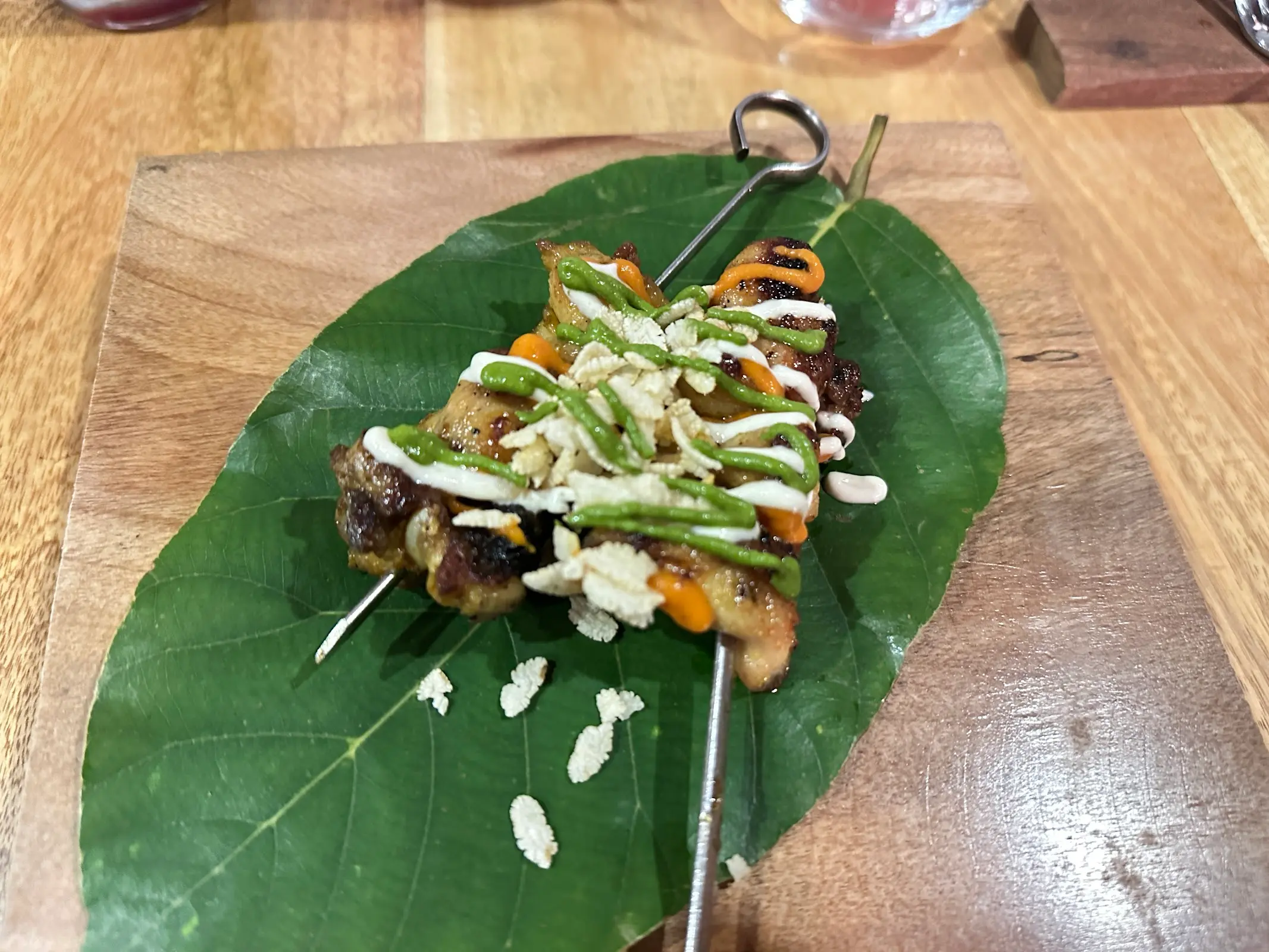 Glazed skewer presented on a sal leaf with crisp puffed rice